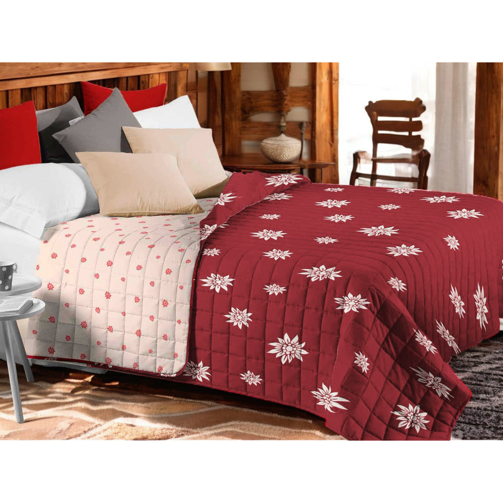 Copriletto trapuntato Edelweiss rosso con fiori bianchi su letto rustico Copriletto trapuntato Edelweiss rosso con fiori bianchi su letto rustico